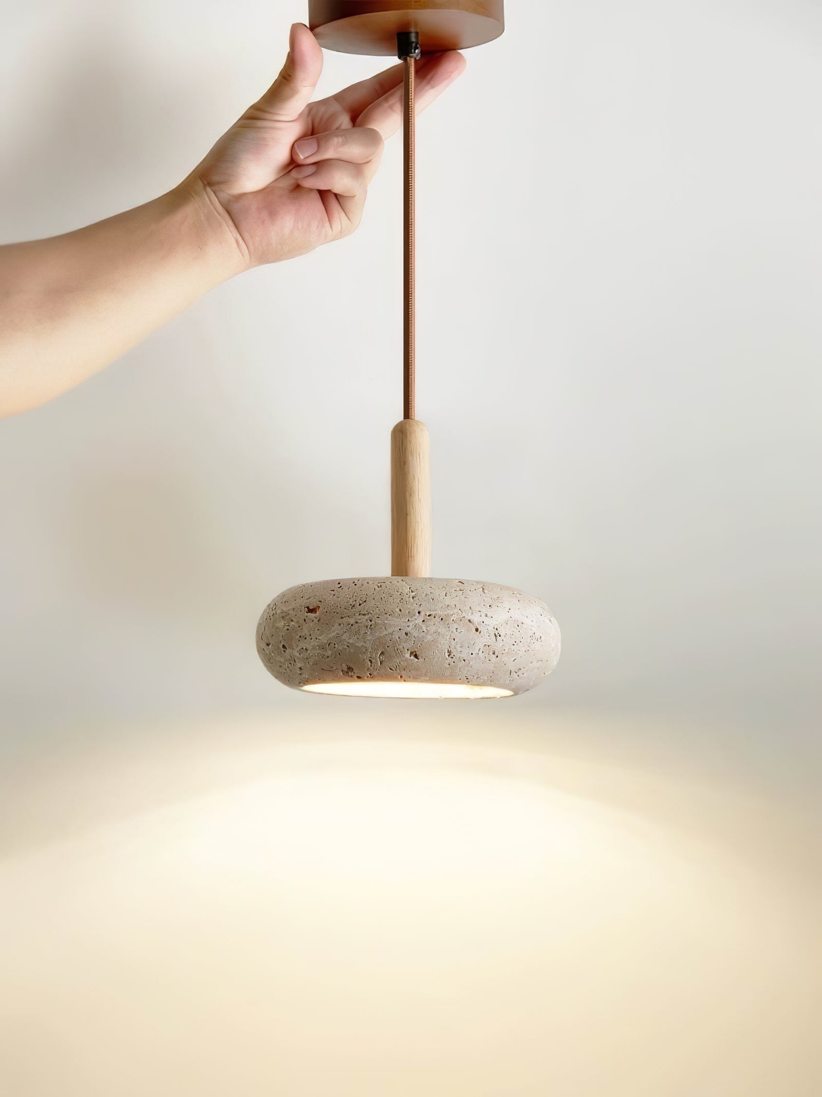 Hand holding the canopy above a suspended travertine pendant