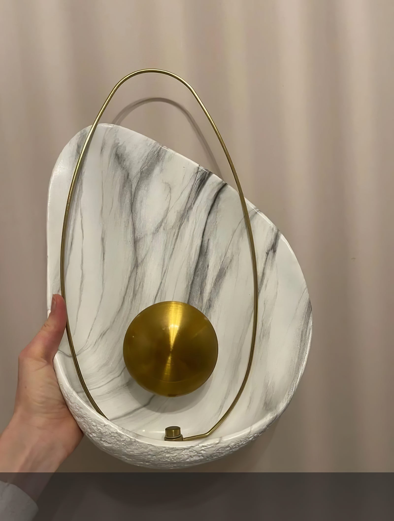 Hand holding the unlit shell-shaped wall lamp