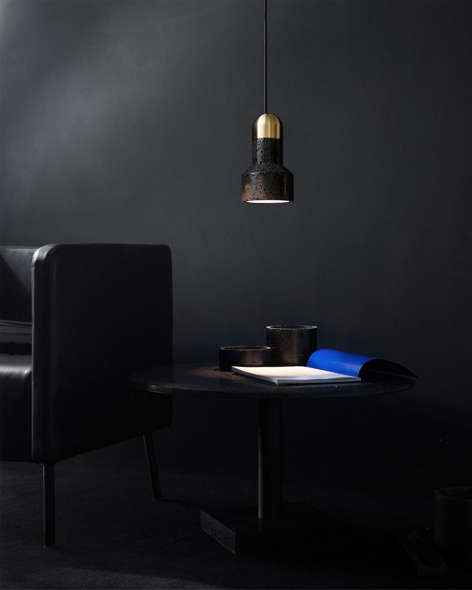 Single textured black pendant beside an armchair and open book