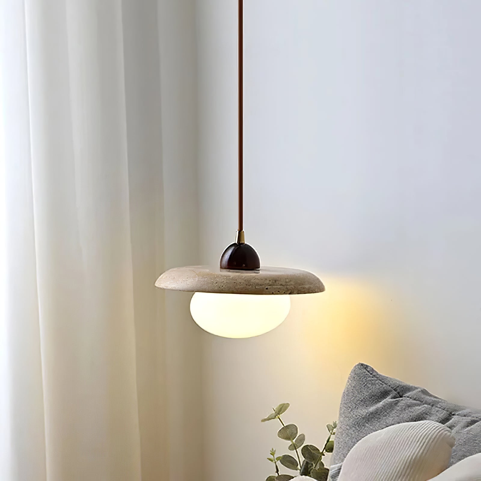 Warm-lit travertine pendant above a bedroom side table