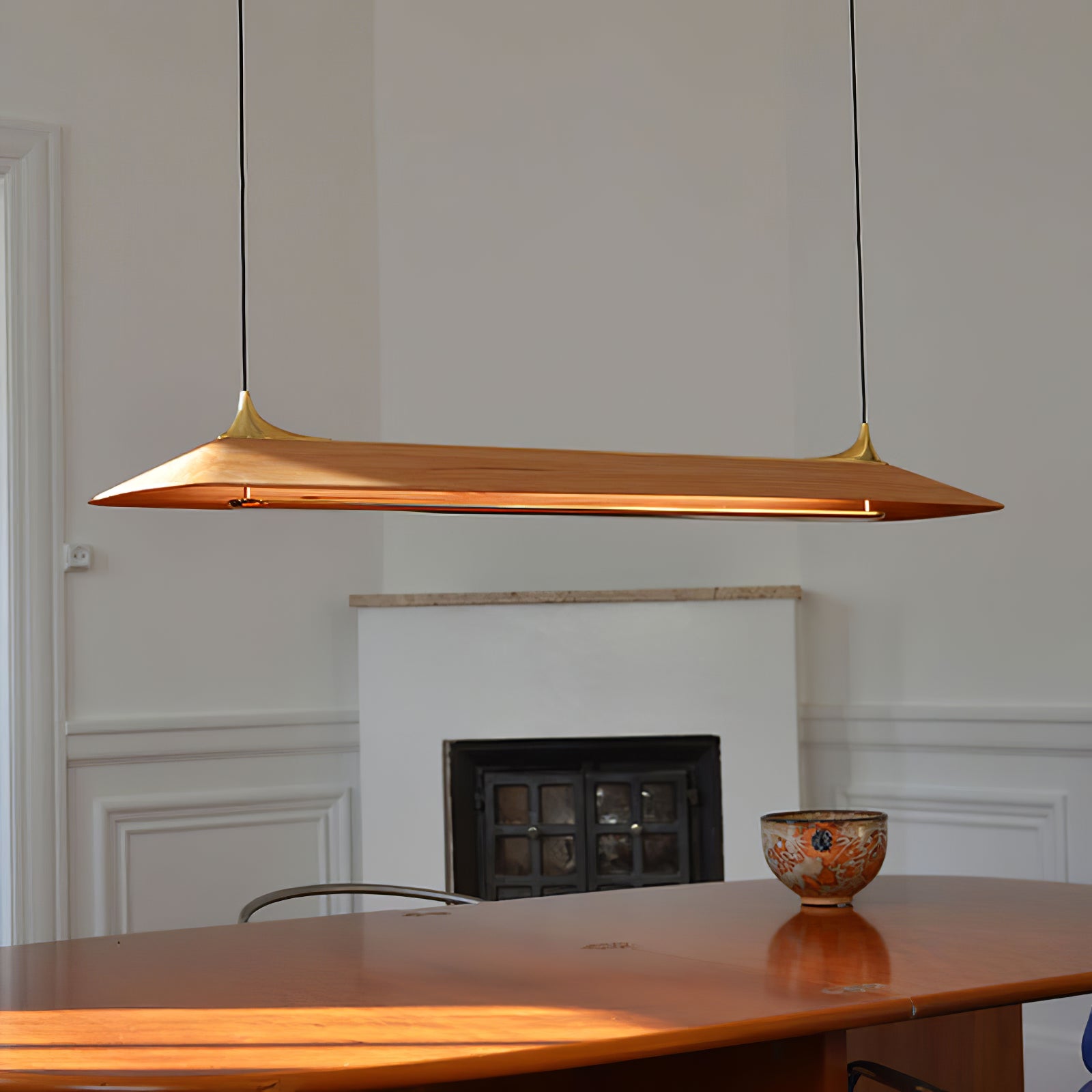 Tapered wood-finish pendant above a table near a fireplace