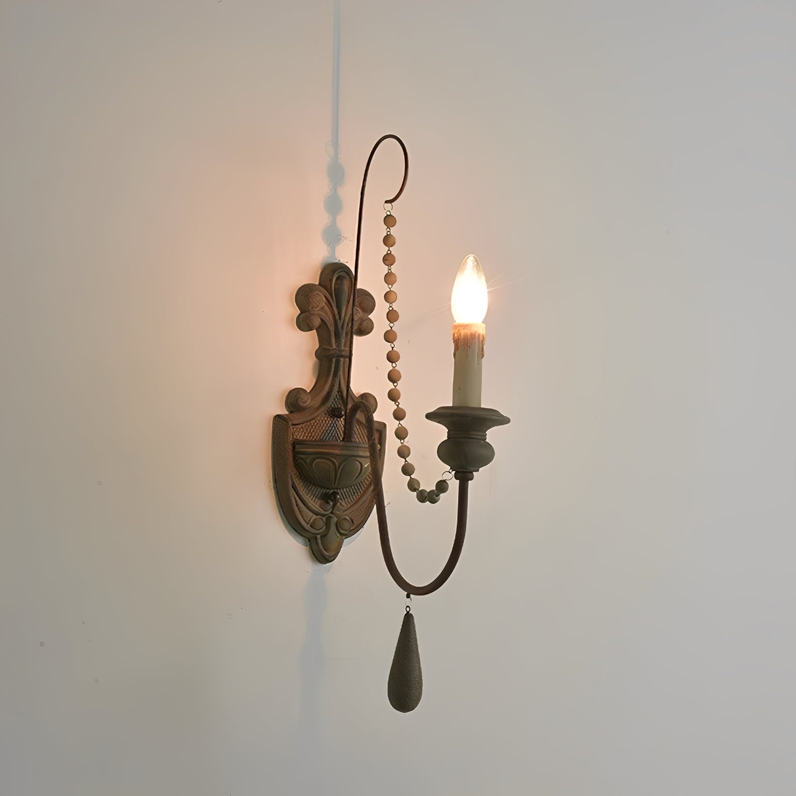 Dark single-arm wall sconce with a carved-look wood backplate and beaded strand