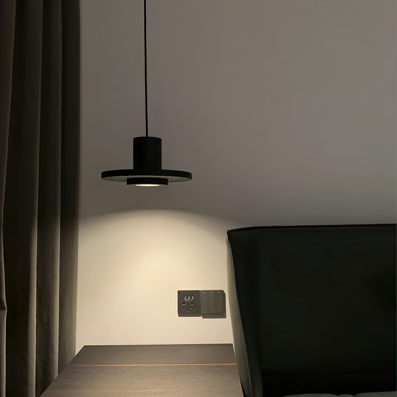 Small black pendant casting light beside a dark headboard