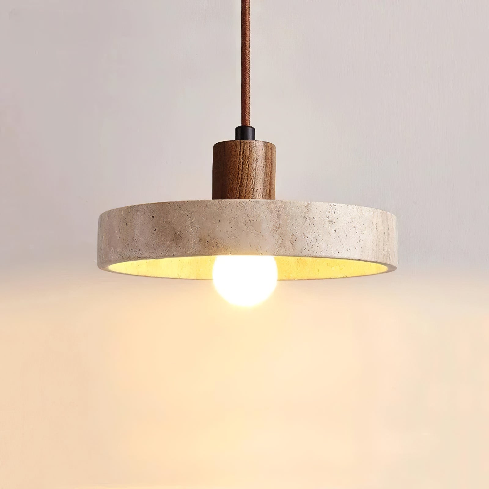 Front view of the lit travertine pendant with dark wooden stem