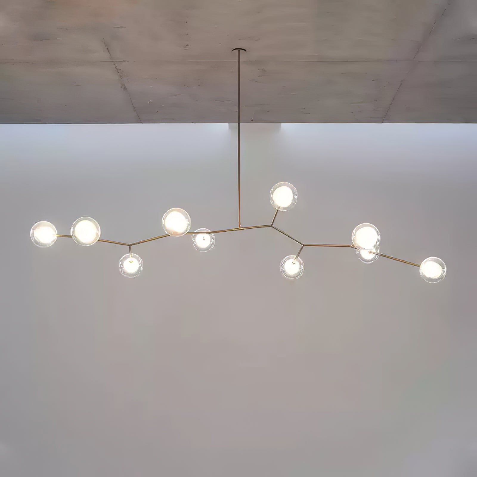 Glass globes along a gold branch frame near a concrete ceiling